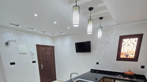A modern kitchen with a black granite countertop, wooden cabinets, a built-in sink, and a compact refrigerator. - STANDING SAIDIA APARTMENT (Saïdia)