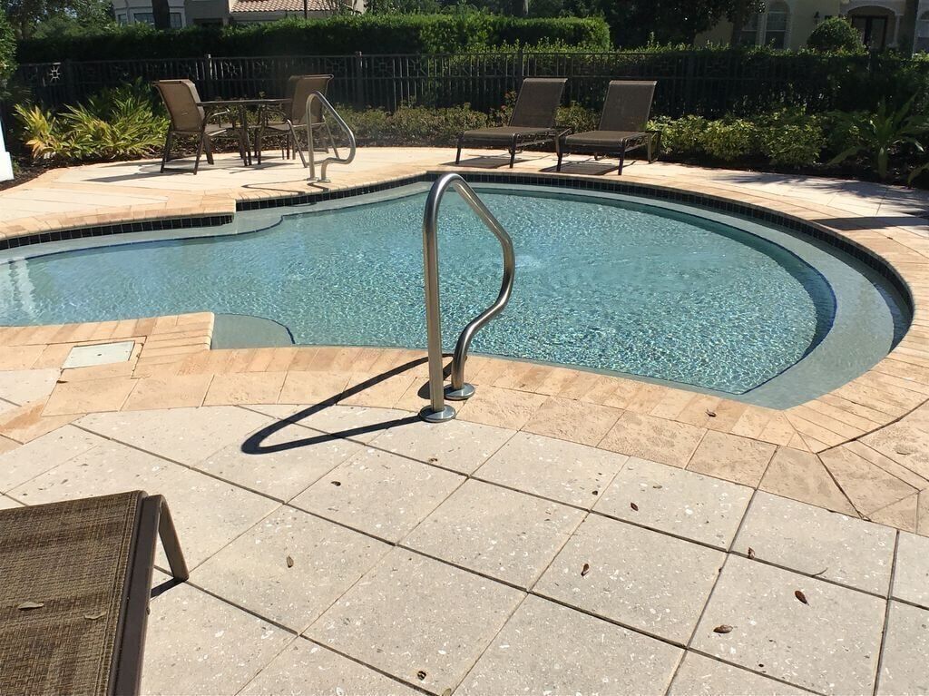 Una piscina con una escalera metálica, sillas de descanso y una terraza con baldosas.