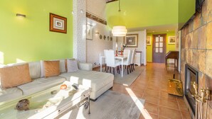 Amplia sala de estar con sofá, mesa de comedor y sillas, chimenea y escalera que sube a un nivel superior.