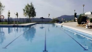 Piscina con agua cristalina, rodeada por una valla, árboles y vistas a la montaña.