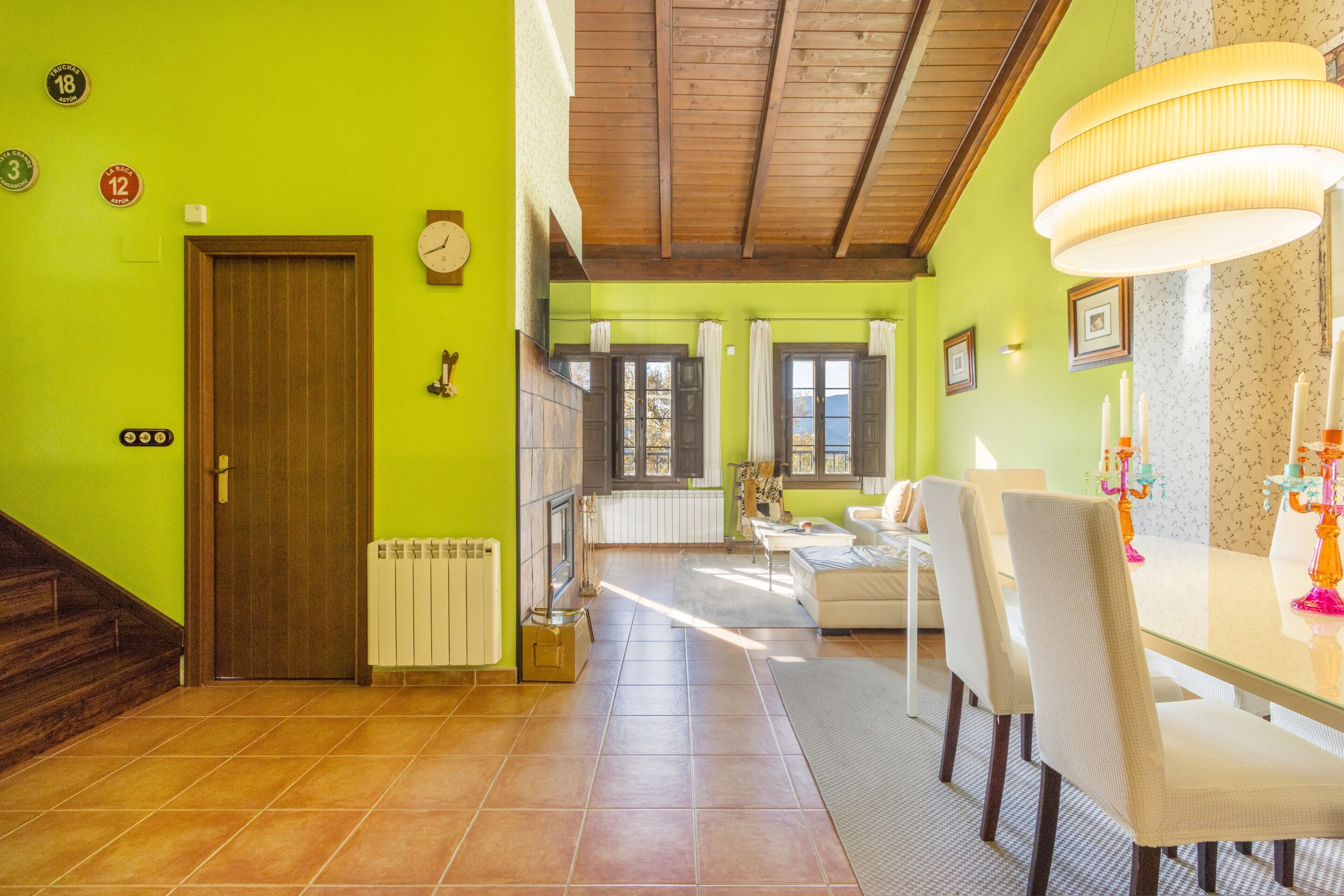 A room with a wooden door, a radiator, a fireplace, a dining table with chairs, and a large window with curtains.