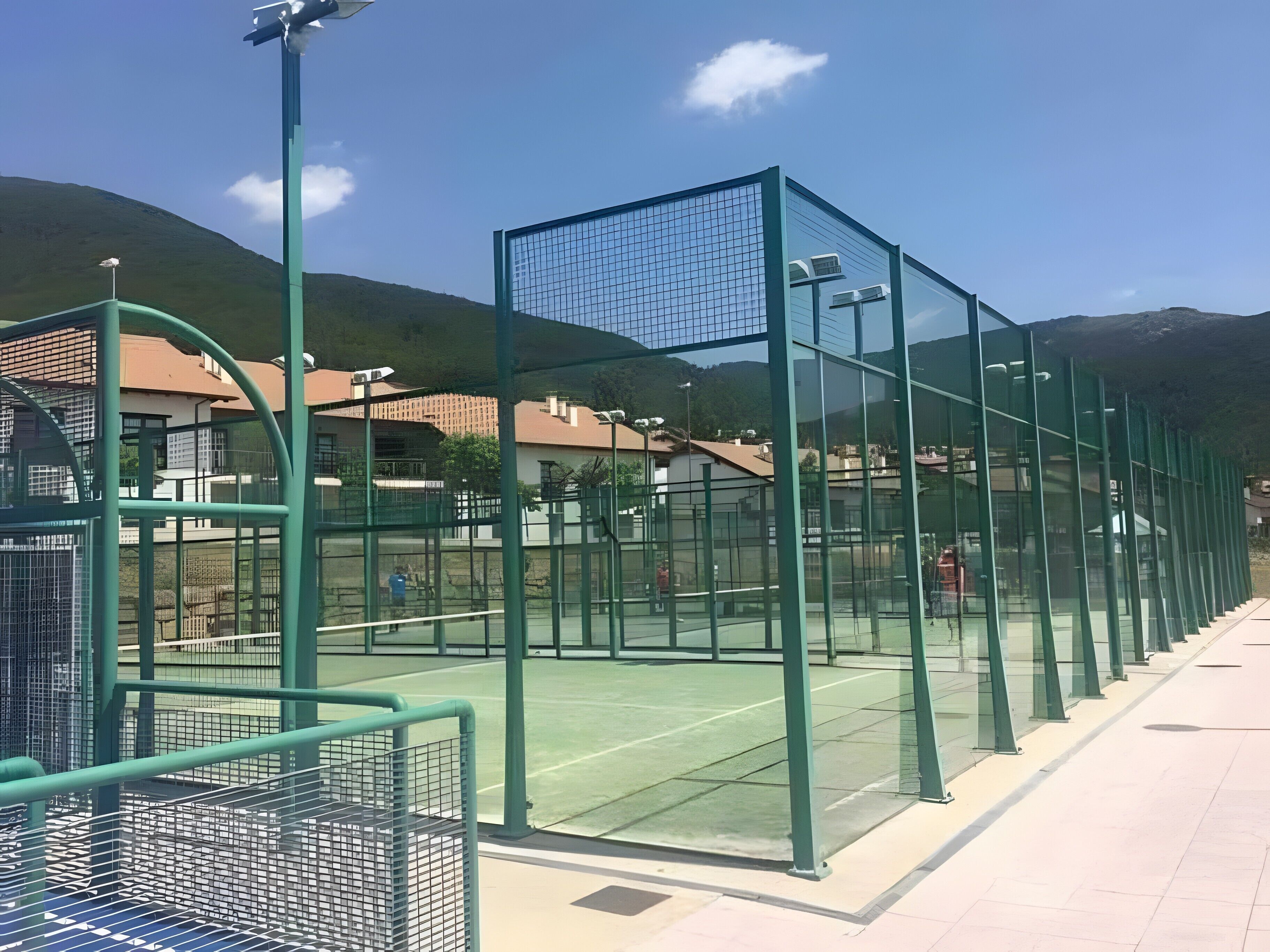 A tennis court with a green fence, a net, and a clear sky.