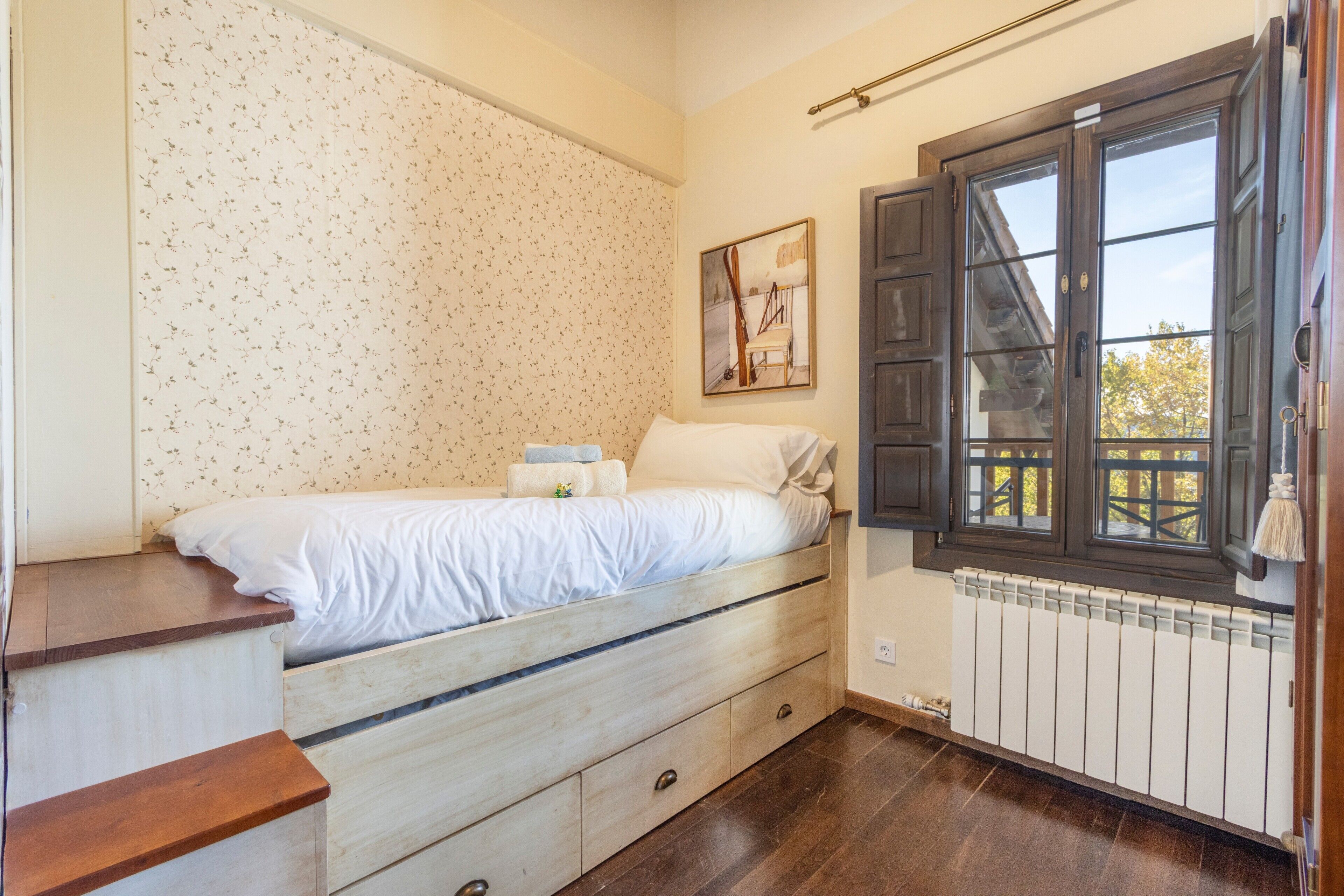 A bedroom with a bed, wooden drawers, a radiator, and a window with shutters.