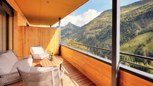 Un balcón con muebles de mimbre, piso de madera y vistas a un paisaje montañoso.