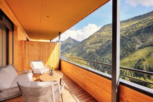 Un balcón con muebles de mimbre, piso de madera y vistas a un paisaje montañoso.