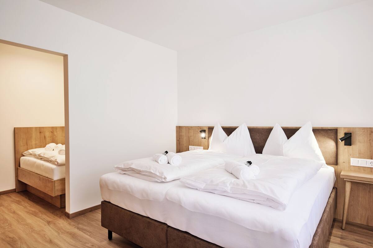 A neatly made bed with white linens and pillows, a wooden headboard, and a bedside table with a lamp.