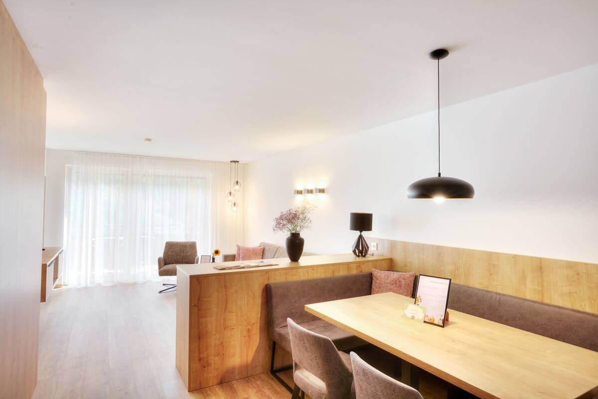 A modern dining area with a wooden table and benches, a vase with flowers, and a pendant light.