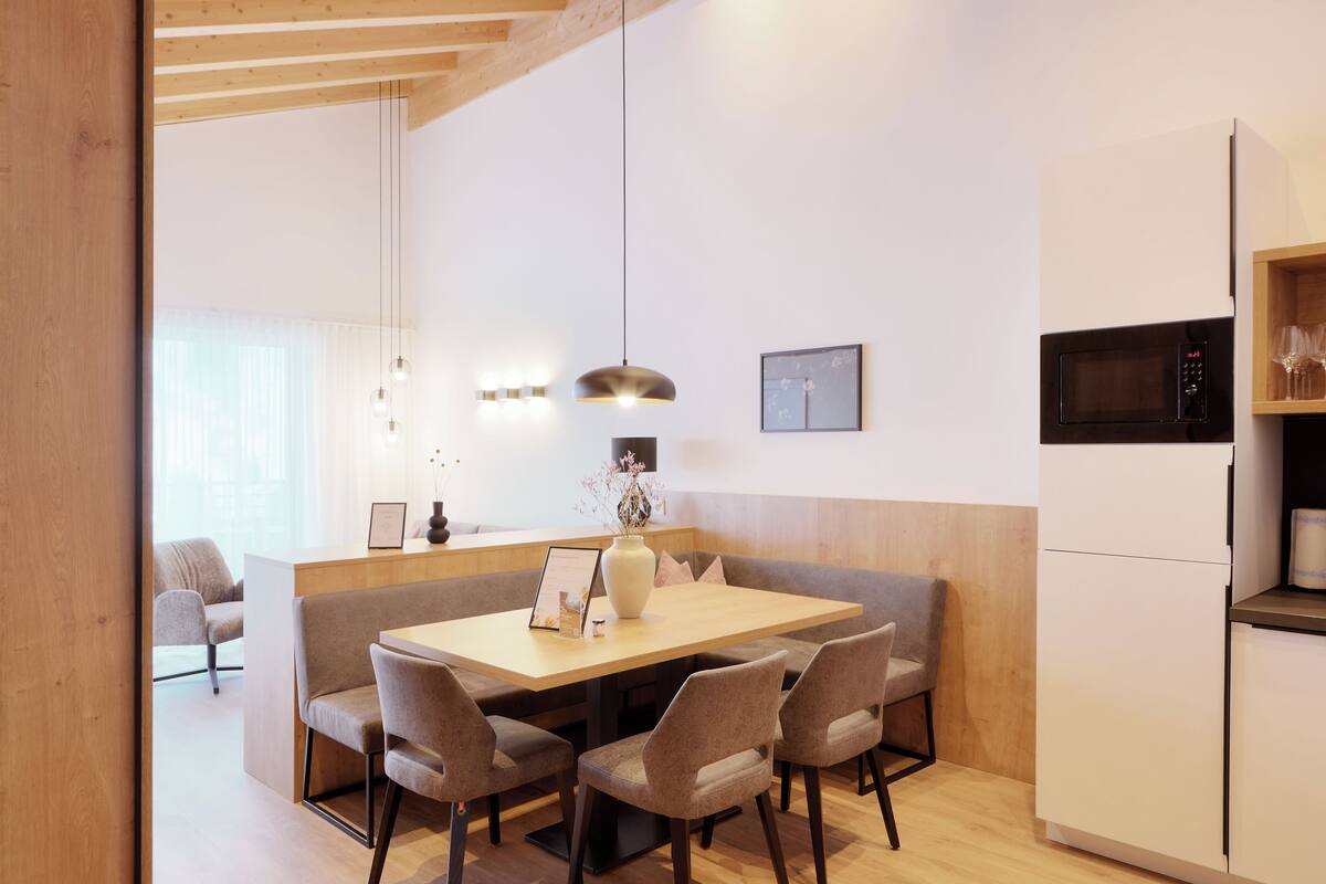 A modern kitchen with a wooden dining table, six chairs, a central island, pendant lighting, a microwave, and a refrigerator.