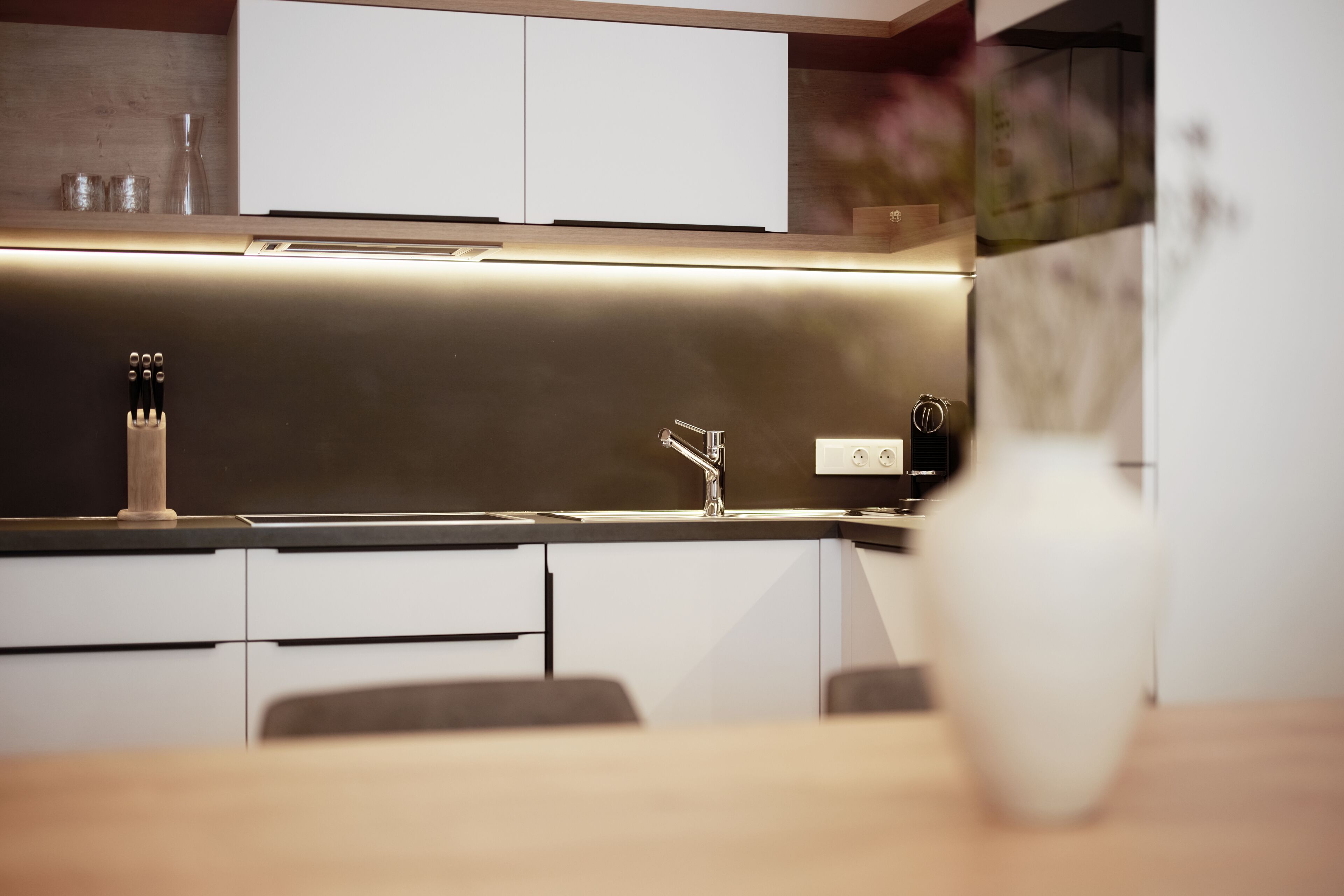 A modern kitchen with white cabinets, a stainless steel sink, and a vase on the counter.
