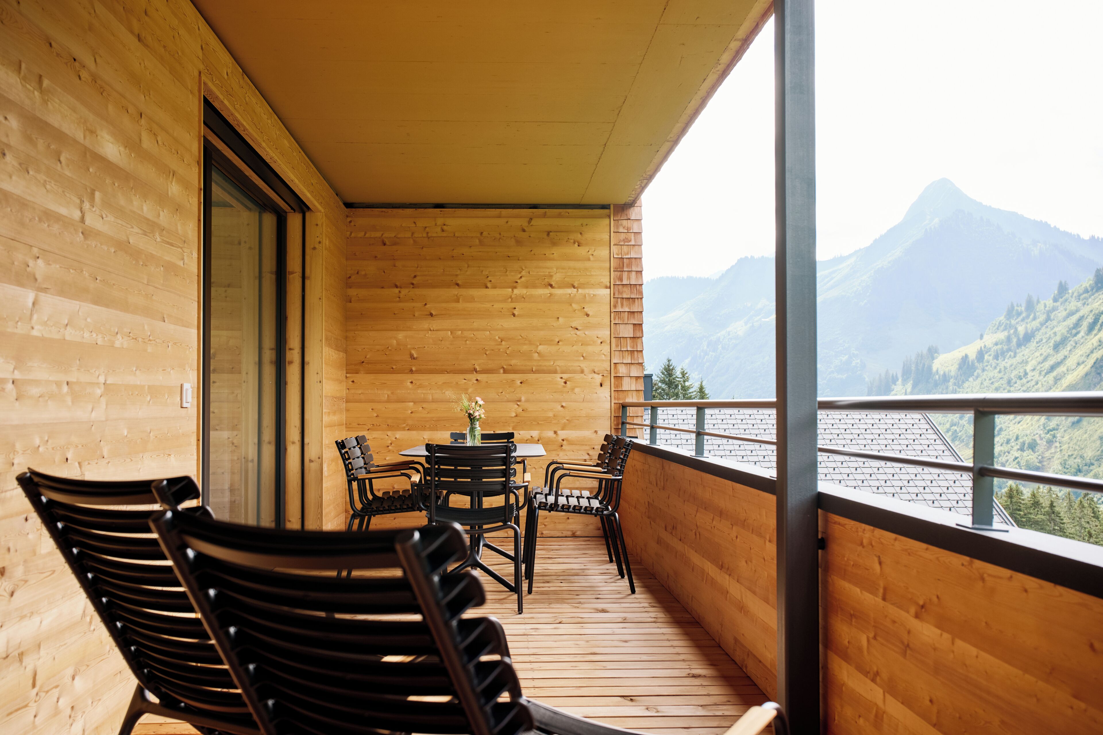 Un balcon en bois, agrémenté d’une table et de chaises, qui offre une vue sur un paysage montagneux.