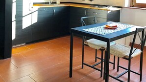 Una cocina con gabinetes oscuros, salpicadero de azulejos, un colgador para ollas y un comedor con sillas.