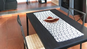 Una sala de estar con chimenea, una mesa de comedor con un mantel individual, un sofá, un escritorio y una estantería.