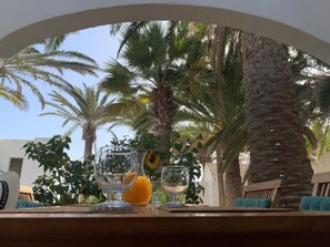 A table with a glass of orange juice and a glass of white wine, set against a backdrop of palm trees and a building.