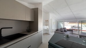 Eine moderne Küche mit einem schwarzen Spülbecken, weißen Schränken und einem Essbereich mit einem grauen Sofa und einem Tisch.