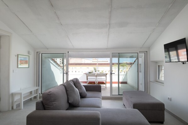 A modern living room with a grey sofa, a bench, and a flat-screen TV mounted on the wall.