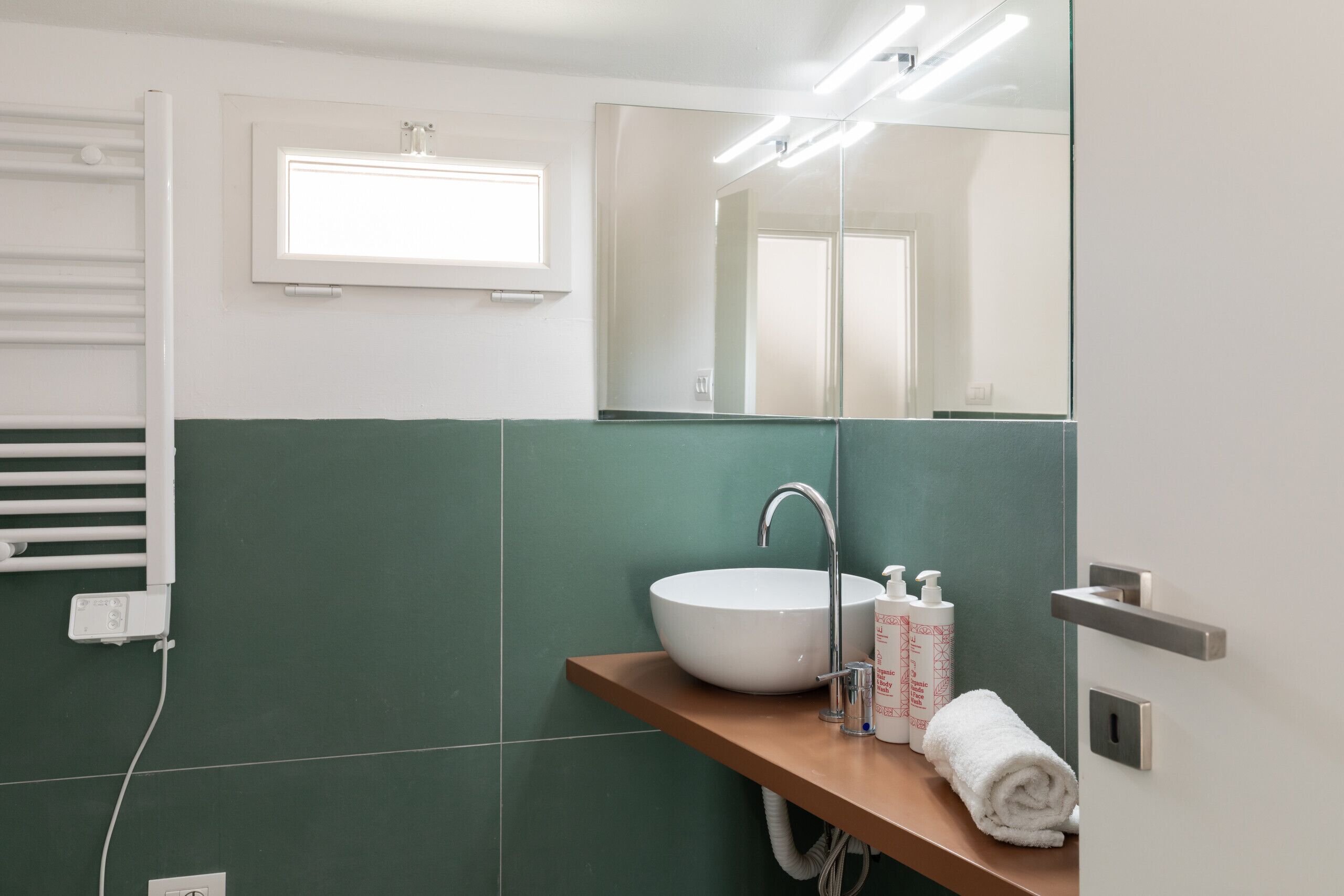 Une salle de bain avec un lavabo blanc, un miroir, une serviette et une fenêtre au-dessus du lavabo.