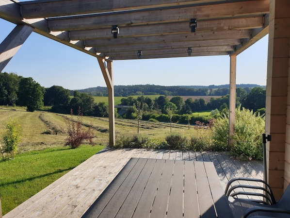 A wooden deck with a view of a green landscape and a bridge in the distance.