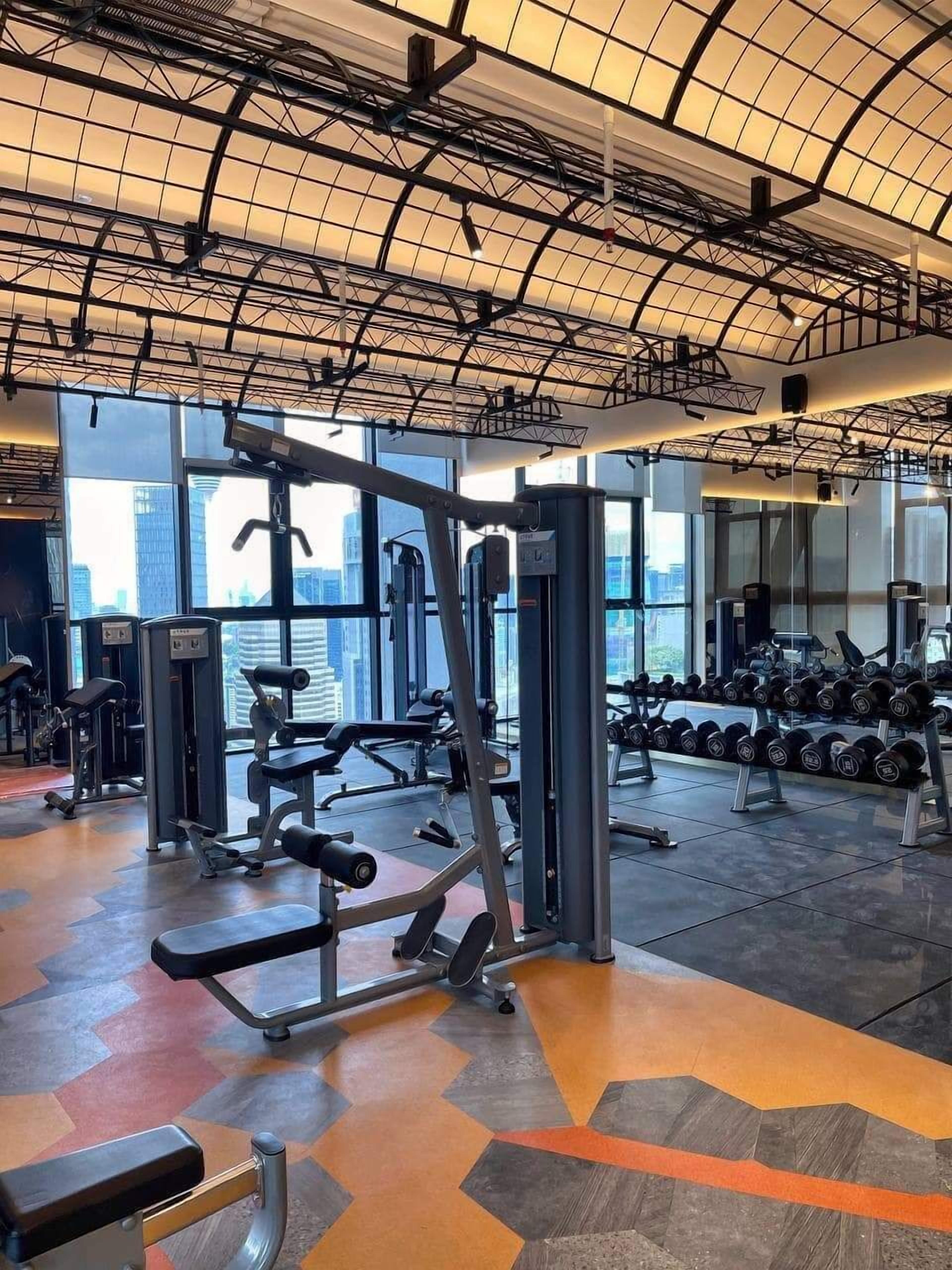 A gym with various exercise equipment, large windows, and a patterned floor.