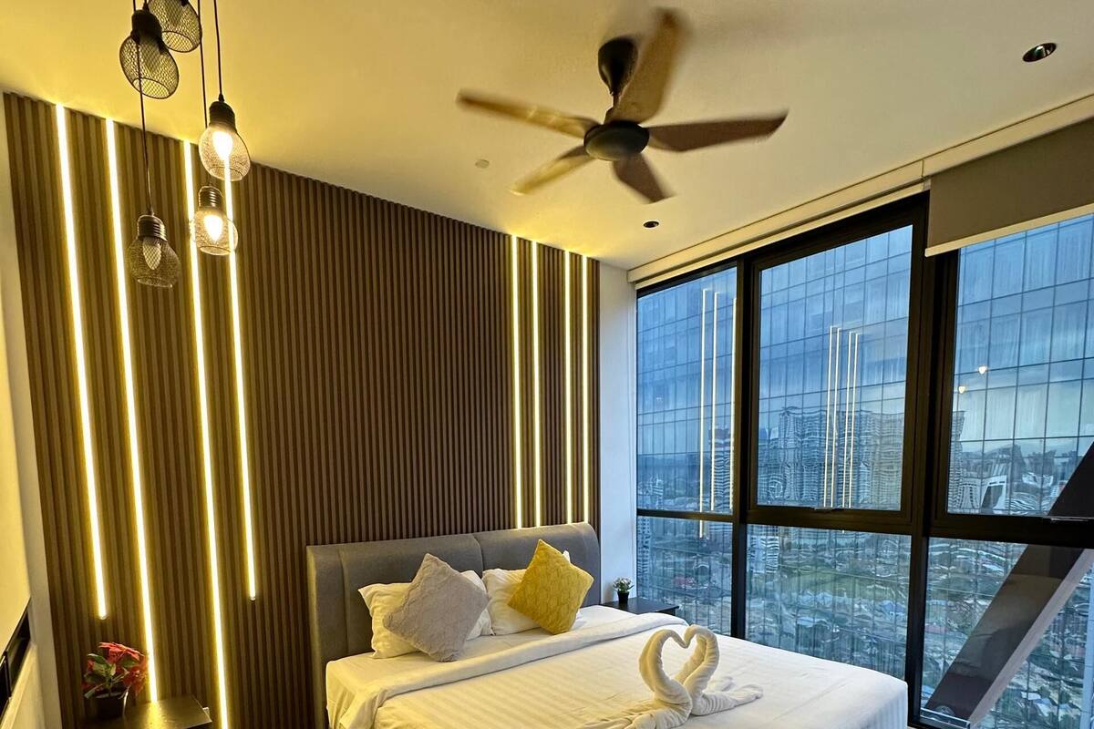 A modern bedroom with a large bed, a ceiling fan, and a city view through large windows.