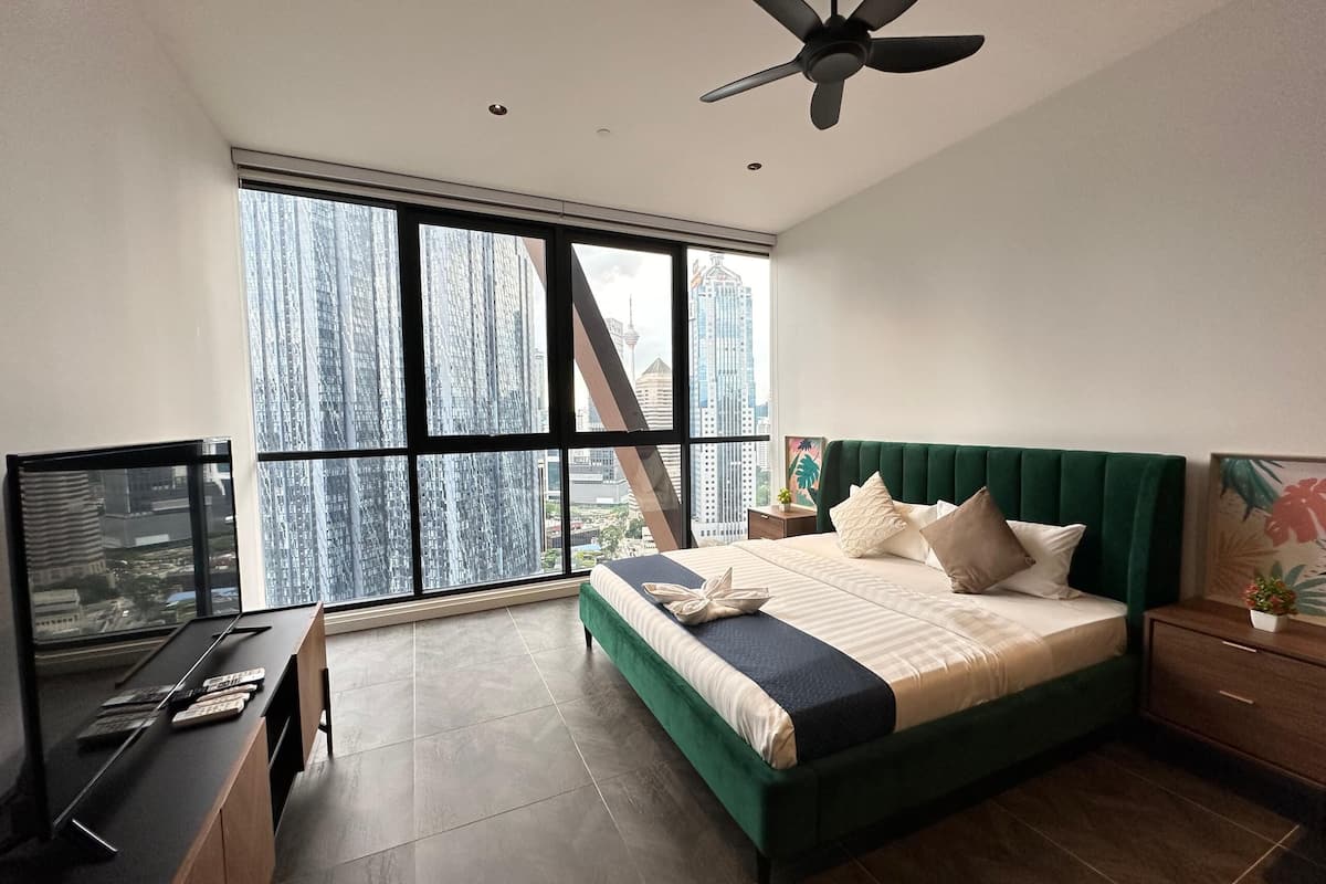 A modern bedroom with a large window, a bed with green headboard, a desk, and a ceiling fan.