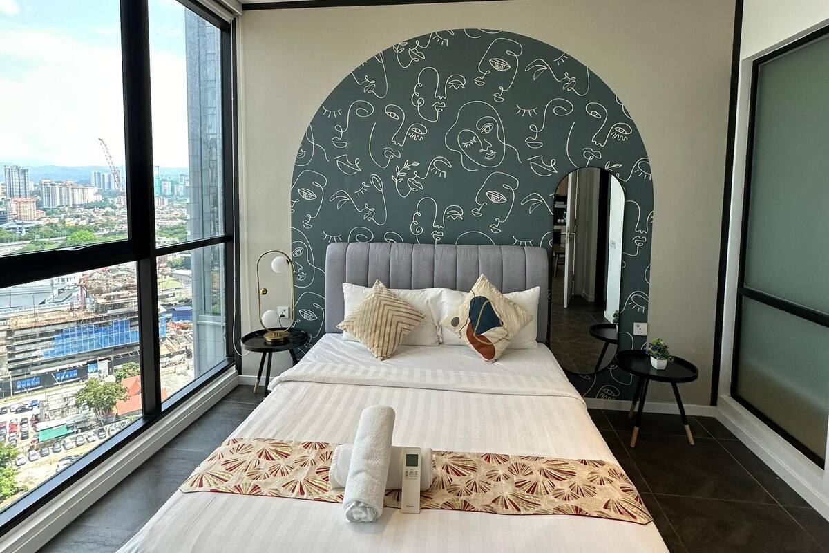 A modern bedroom with a large bed, a ceiling fan, and a city view through large windows.