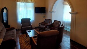 A living room with a sofa, armchairs, a coffee table, a TV, a clock, and a fireplace. - The Hill Cliff Nuwara Eliya (Nuwara eliya)