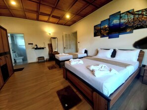Habitación de hotel con una cama grande, dos camas más pequeñas, techo de madera y un baño visible a través de una puerta abierta.