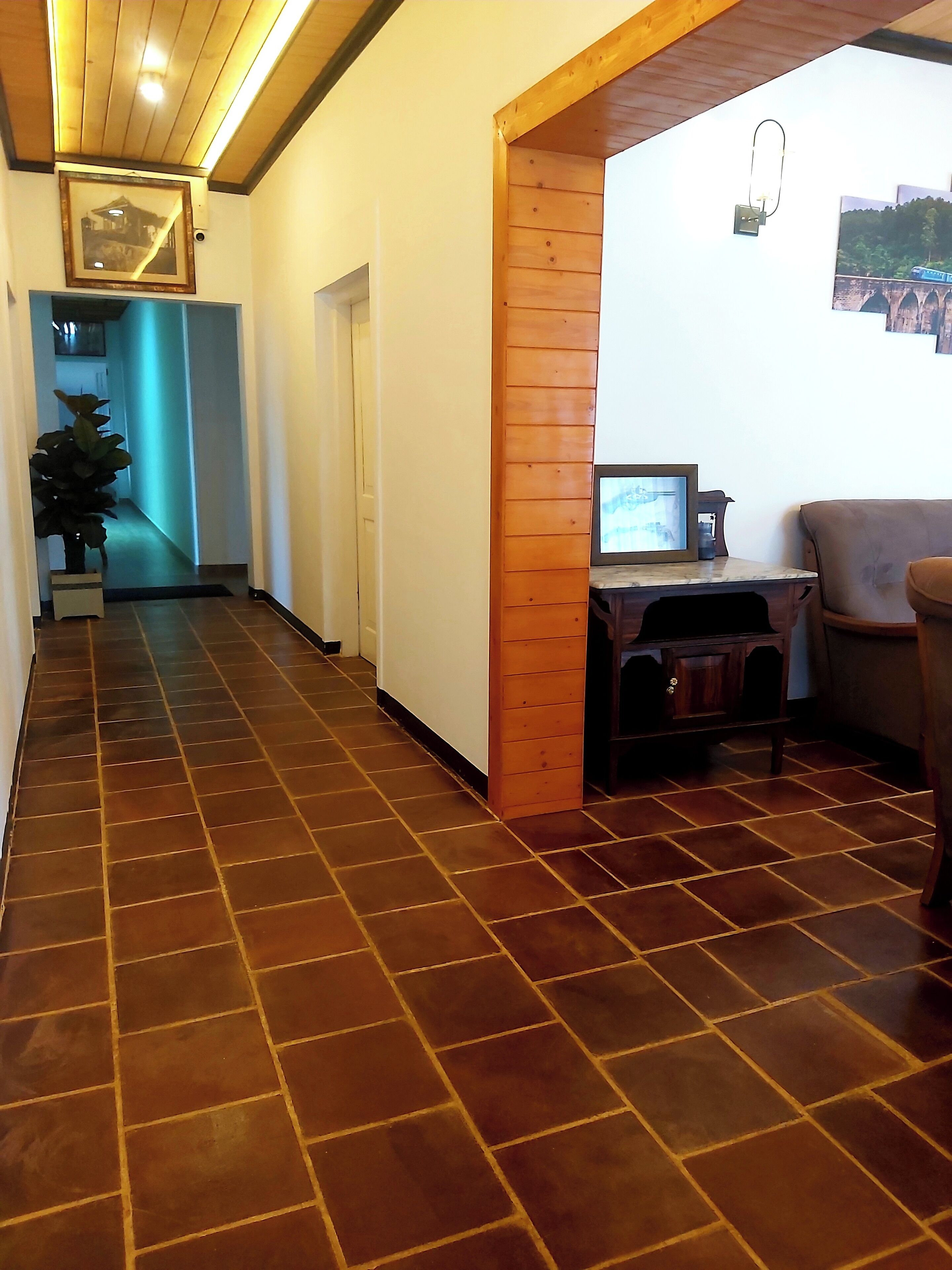 Un pasillo con suelo de baldosas, techo de madera, un escritorio con computadora y una silla.