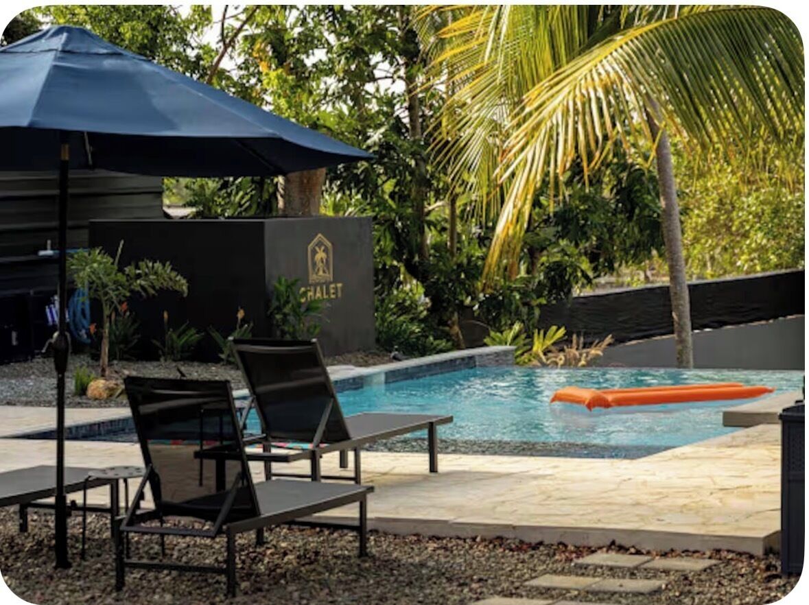A pool area with lounge chairs and an umbrella, surrounded by tropical vegetation.