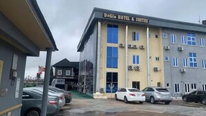 A hotel named DeGio Hotel & Suites with a modern facade, multiple air conditioning units, and a parking lot with several cars. - Degio Hotel and Suites  (Owerri)
