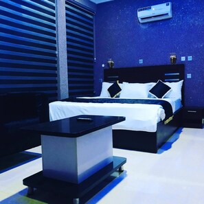 A modern bedroom with a bed, bedside table, and an air conditioning unit. - Degio Hotel and Suites  (Owerri)