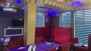 A conference room with a high ceiling, red upholstered chairs, a central table with a purple tablecloth, and a large window with blinds. - Degio Hotel and Suites  (Owerri)