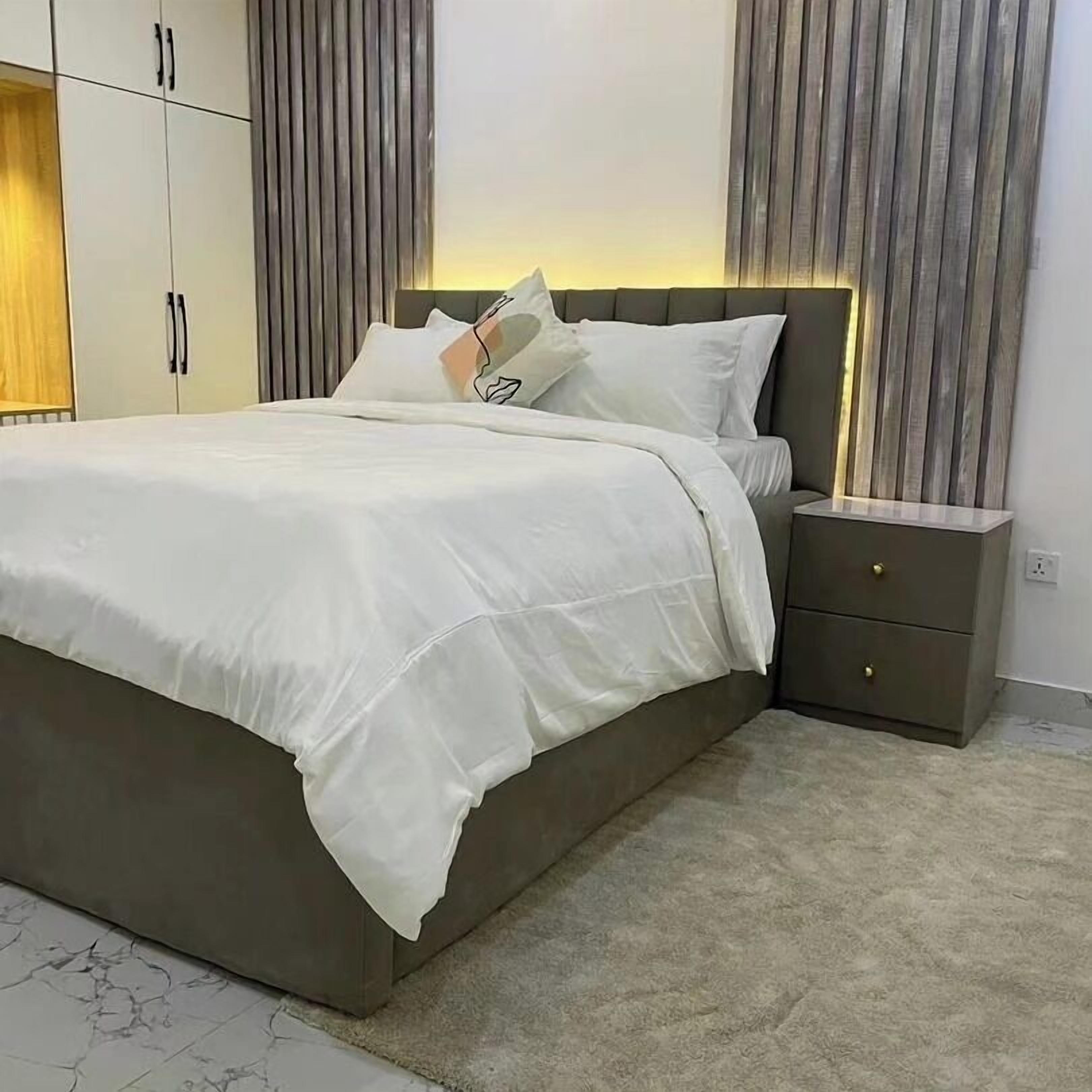 A modern bedroom with a large bed, a nightstand, and a wardrobe.