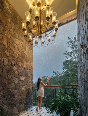 A woman on a balcony with a stone wall and a chandelier. - The Feel Munnar Resort (Devikolam)