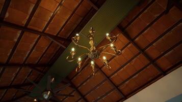 Una habitación con techo de madera, una viga verde y una araña con varias luces.