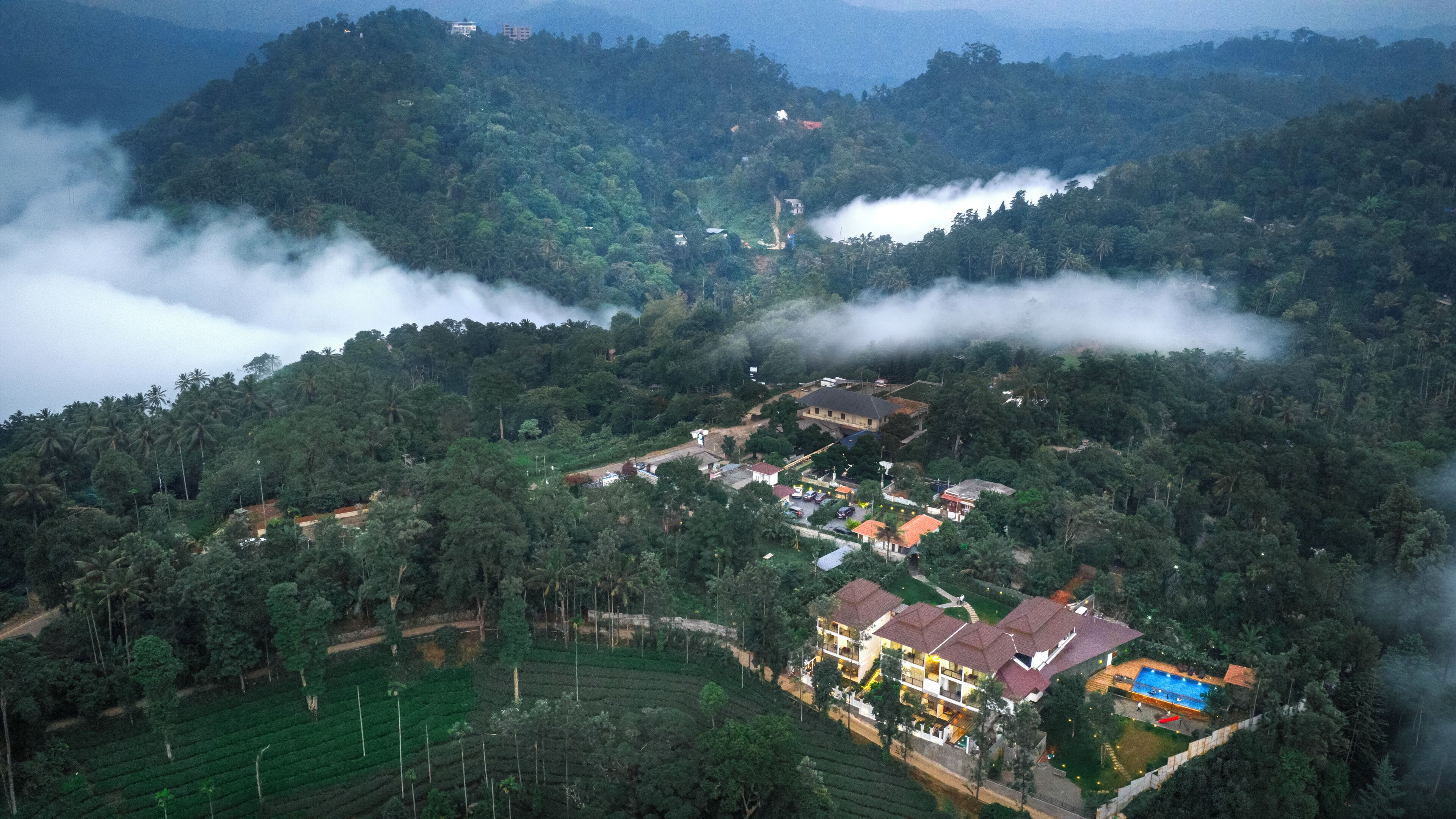 A large building with multiple floors, surrounded by lush greenery and a hilly landscape.