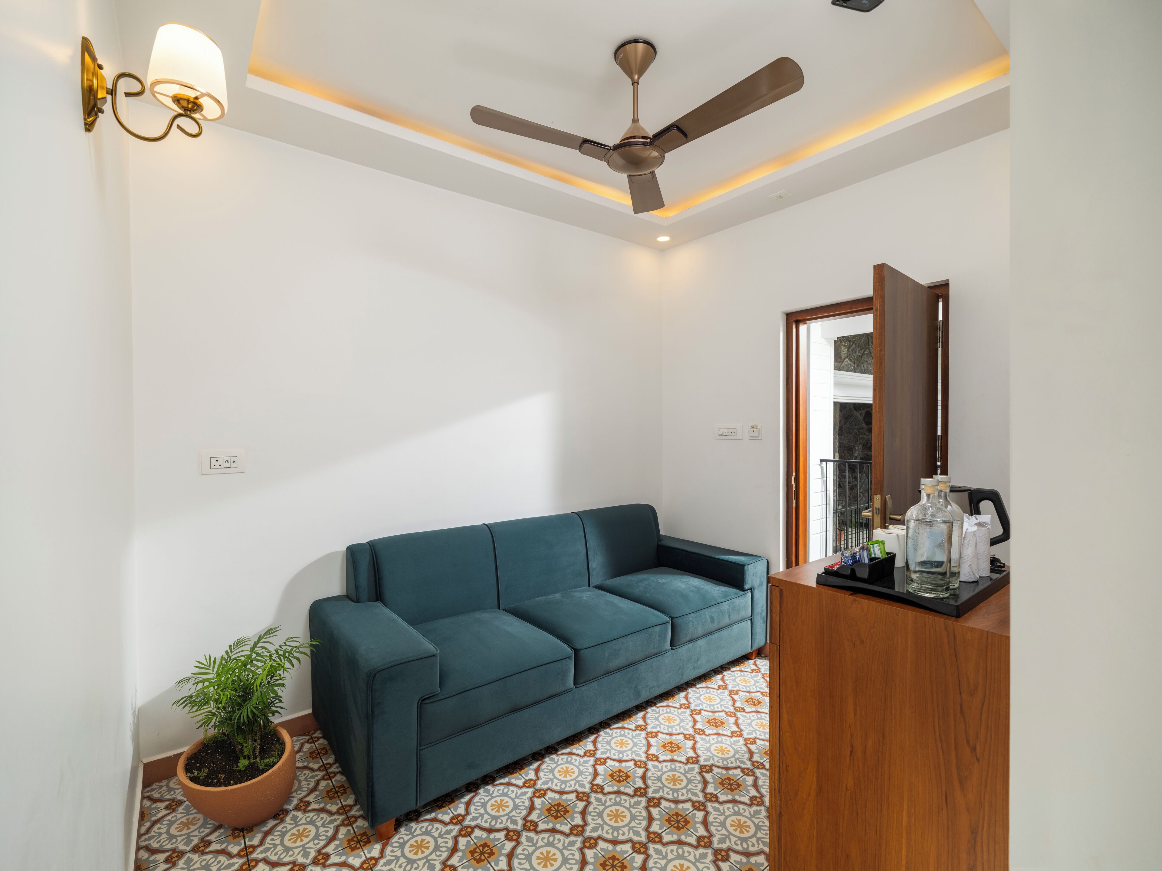 Una sala de estar moderna con un sofá color turquesa, un ventilador de techo, una lámpara empotrada en la pared y una planta en maceta.