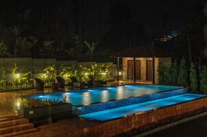 A rectangular swimming pool with a tiled edge, surrounded by a wooden deck and steps leading down to the water. There are lounge chairs and potted plants around the pool area.