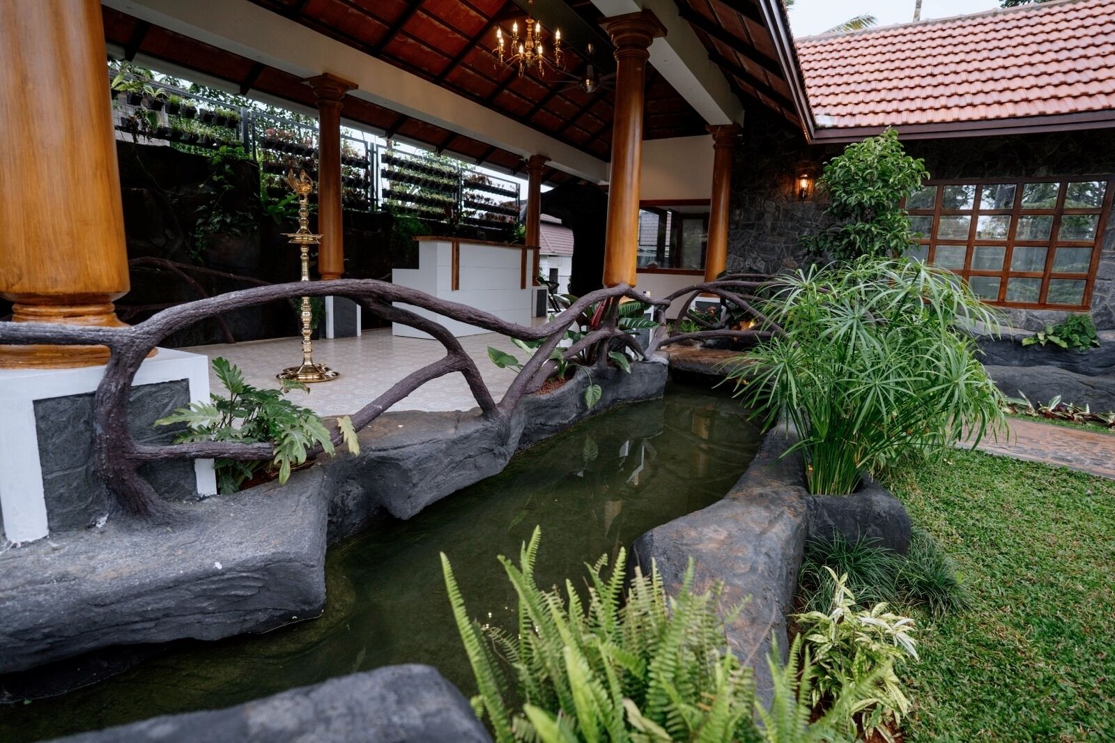A tranquil indoor garden with a water feature, stone bridge, and lush greenery.