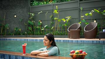 A poolside area with a person leaning on the edge, a drink, and a fruit basket.