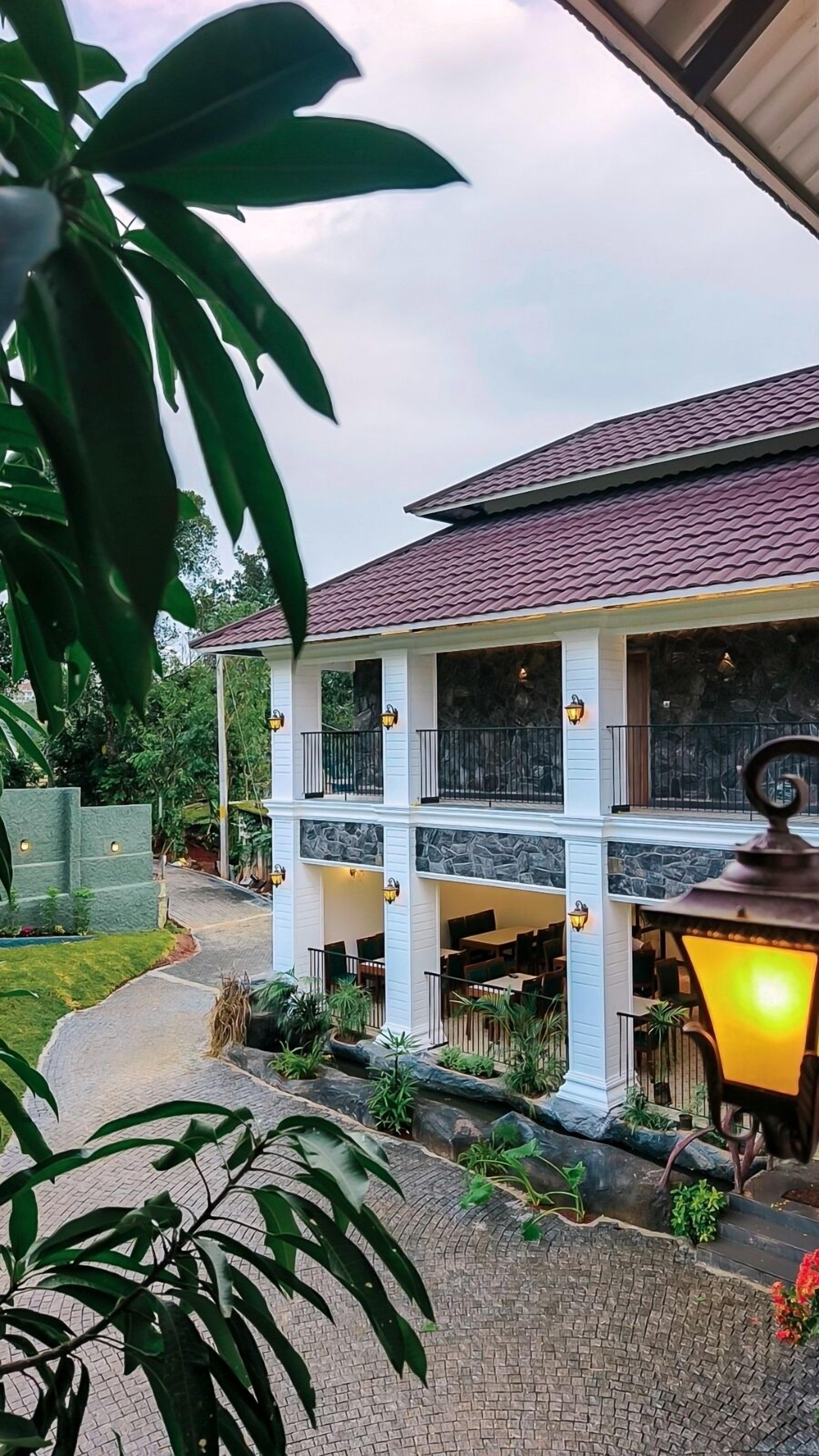 A two-story house with a stone facade, a red-tiled roof, and a covered patio area with outdoor seating.