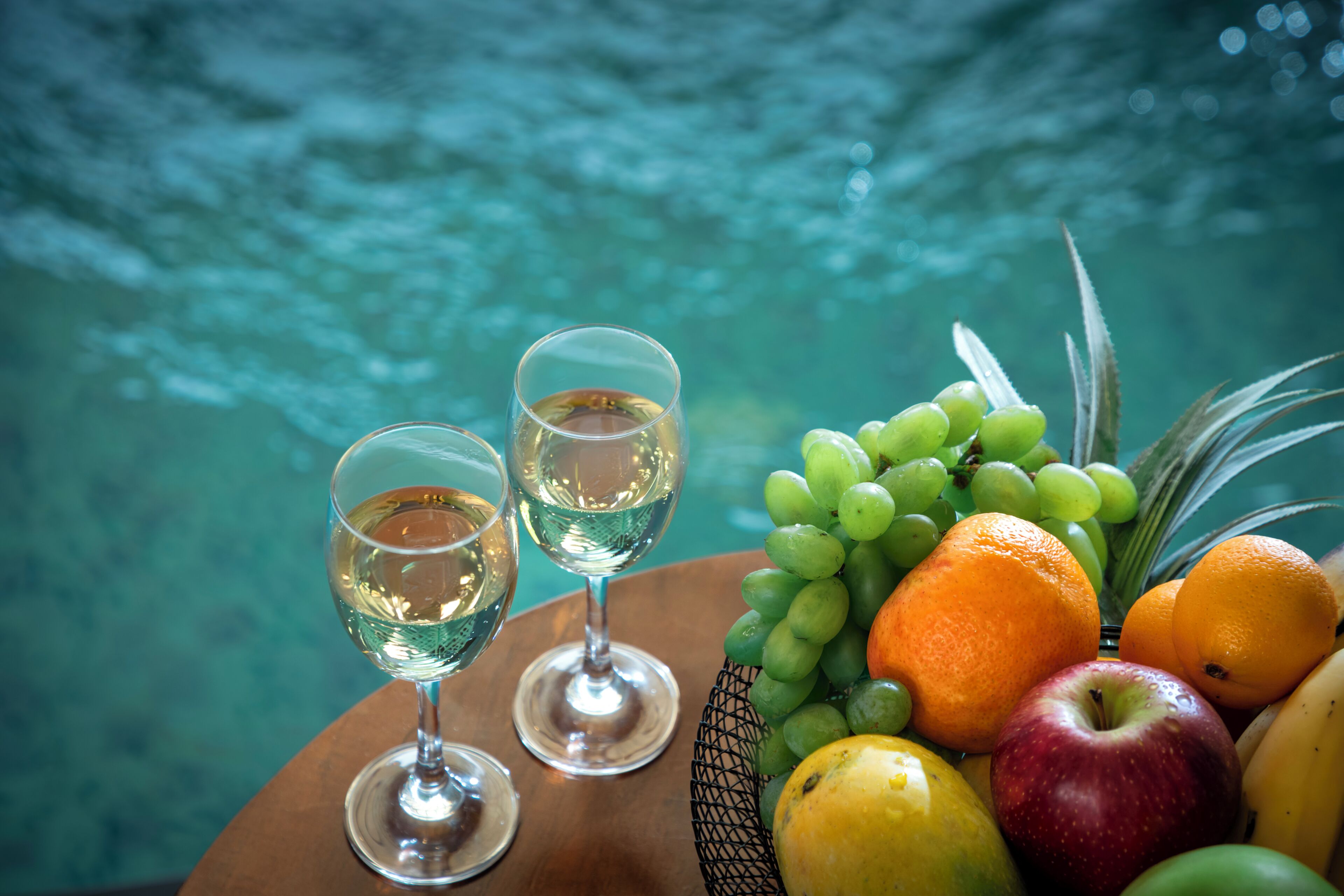 Una mesa con dos copas de vino blanco y un frutero.