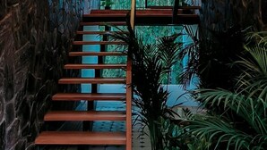A staircase with wooden steps and a metal railing, leading to a balcony with a stone wall and a view of trees. - The Feel Munnar Resort (Devikolam)
