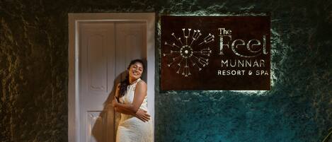 A woman in a white dress standing in front of a door with a sign that reads "The Feel Munnar Resort & Spa".