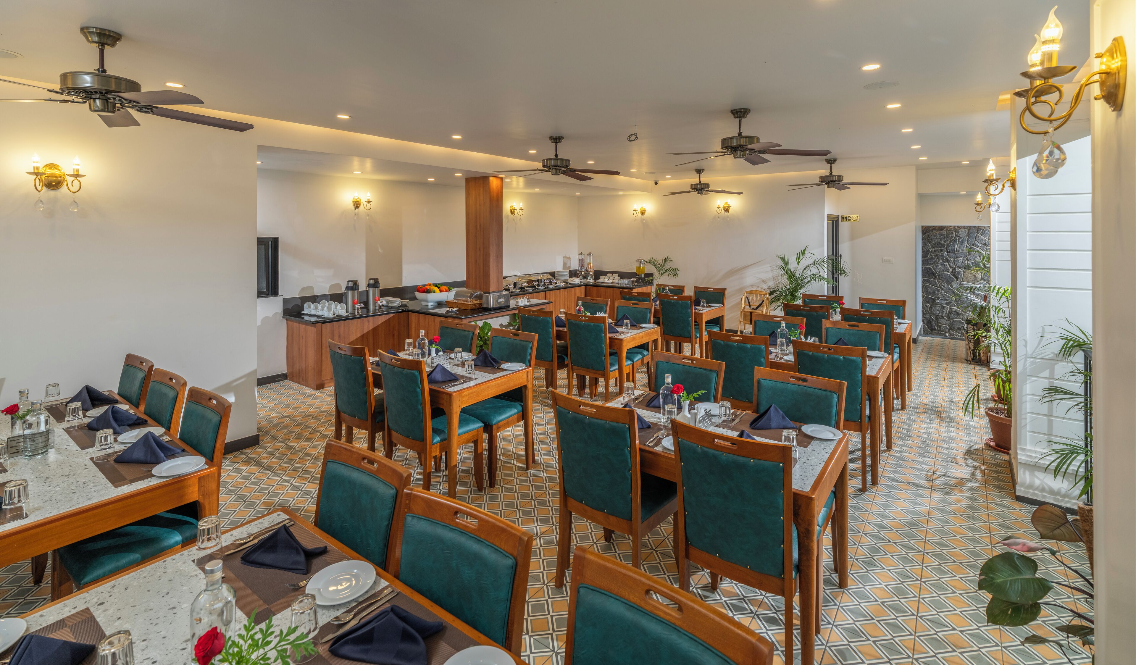 Een restaurantgedeelte in een hotel met meerdere tafels en stoelen, plafondventilatoren en wandlampen.