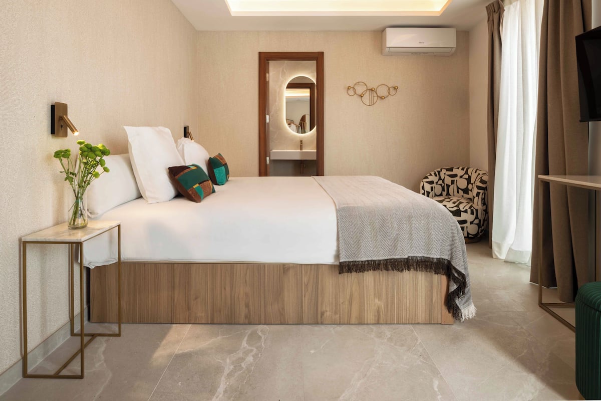 A modern bedroom with a bed, bedside table, mirror, wall art, and a TV.