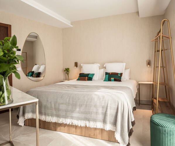A modern hotel room with a large bed, bedside tables, a mirror, a plant, and a ladder.