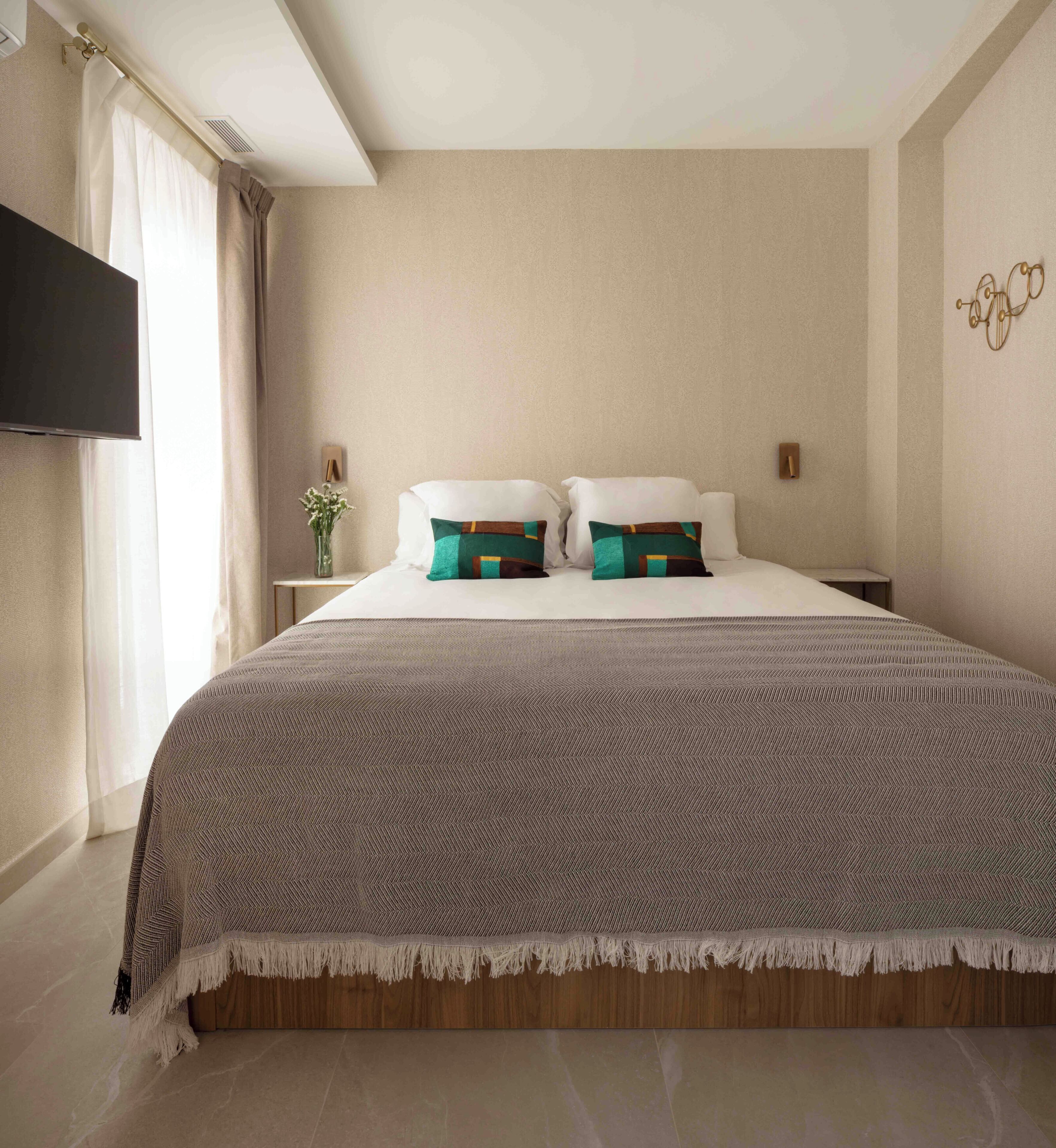 Una habitación de hotel con una cama grande, un televisor de pantalla plana en la pared y una mesita de noche con un jarrón de flores.