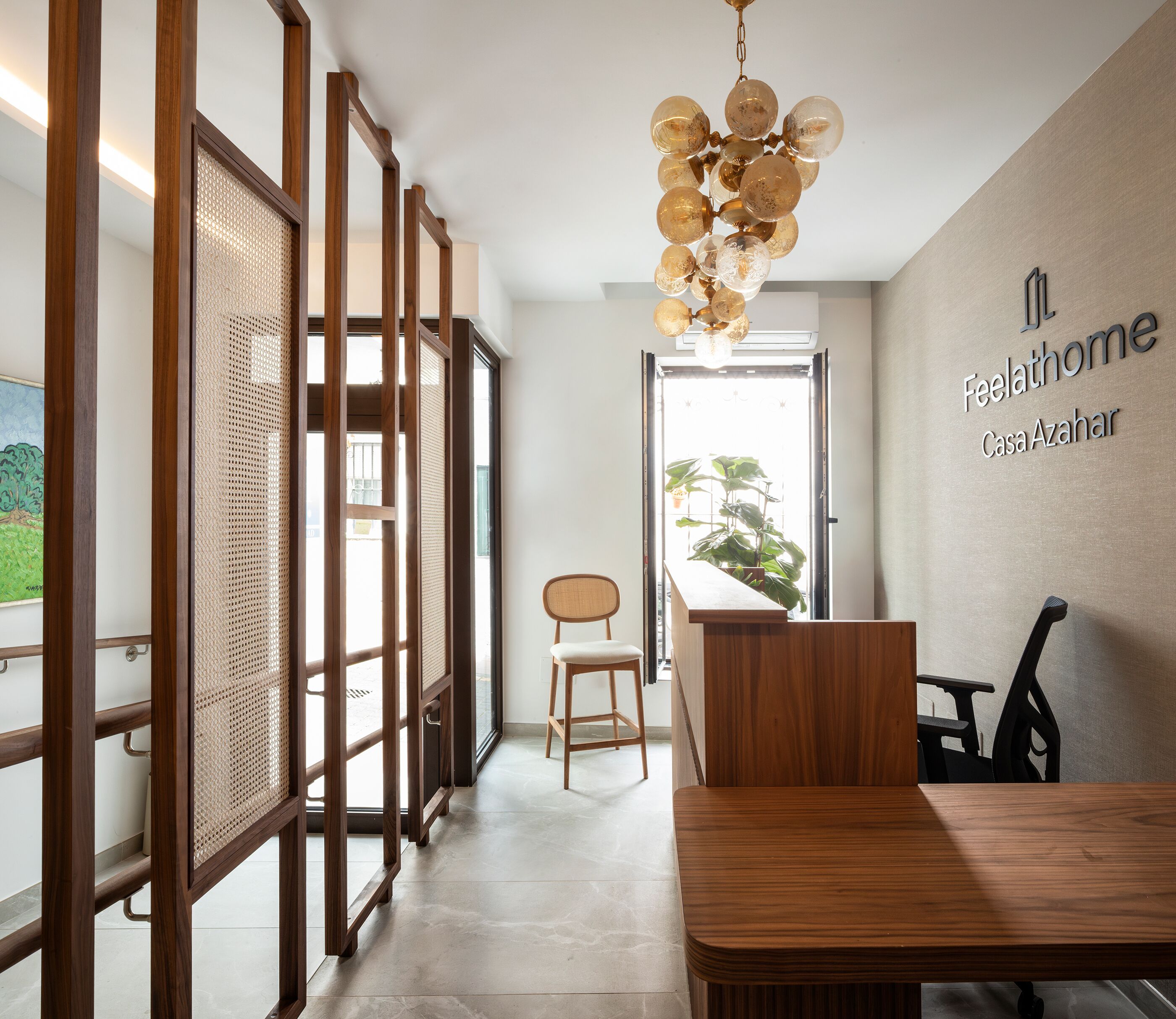 Een modern interieur met een houten receptiebalie, een stoel, een hanglamp en een bord met de tekst 'Feelathome Casa Azahar'.