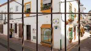 Un bâtiment blanc avec un toit recouvert de tuiles, un balcon orné de plantes en pot et une enseigne indiquant « Calle Huerto ».